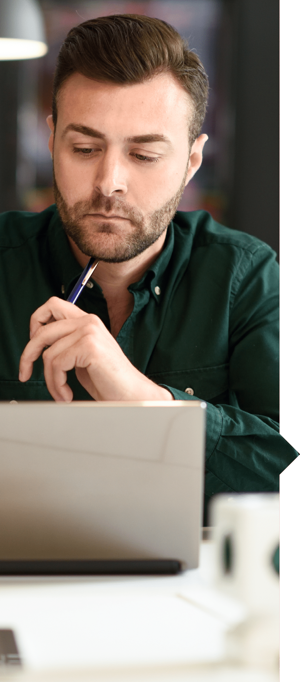 Young man studying with laptop computer on white desk. Attractive guy with beard wearing casual clothes.